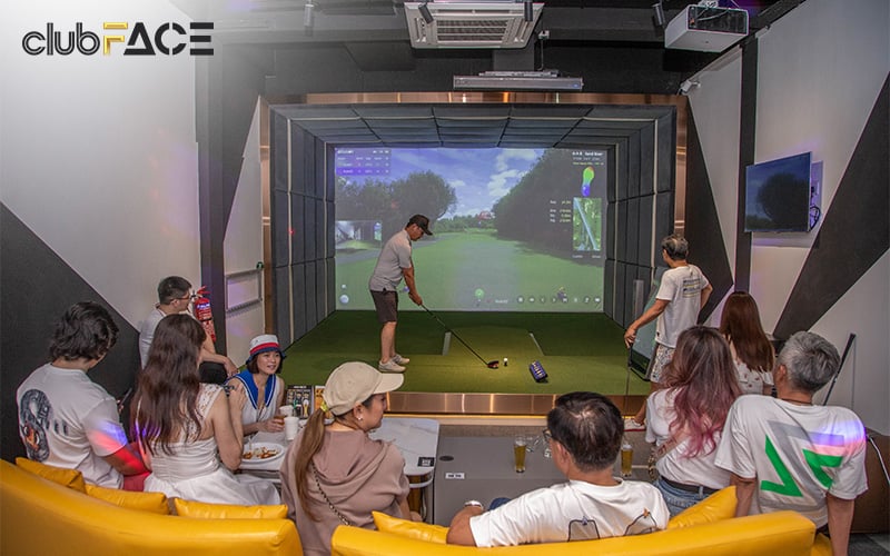Indoor golf simulator with group watching player swing at virtual course