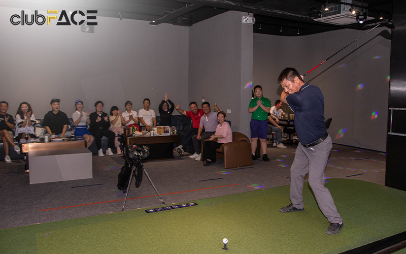 group of people having fun watching a man play the golf simulator